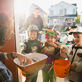 Young costumed trick or treaters in an open doorway, receiving candy